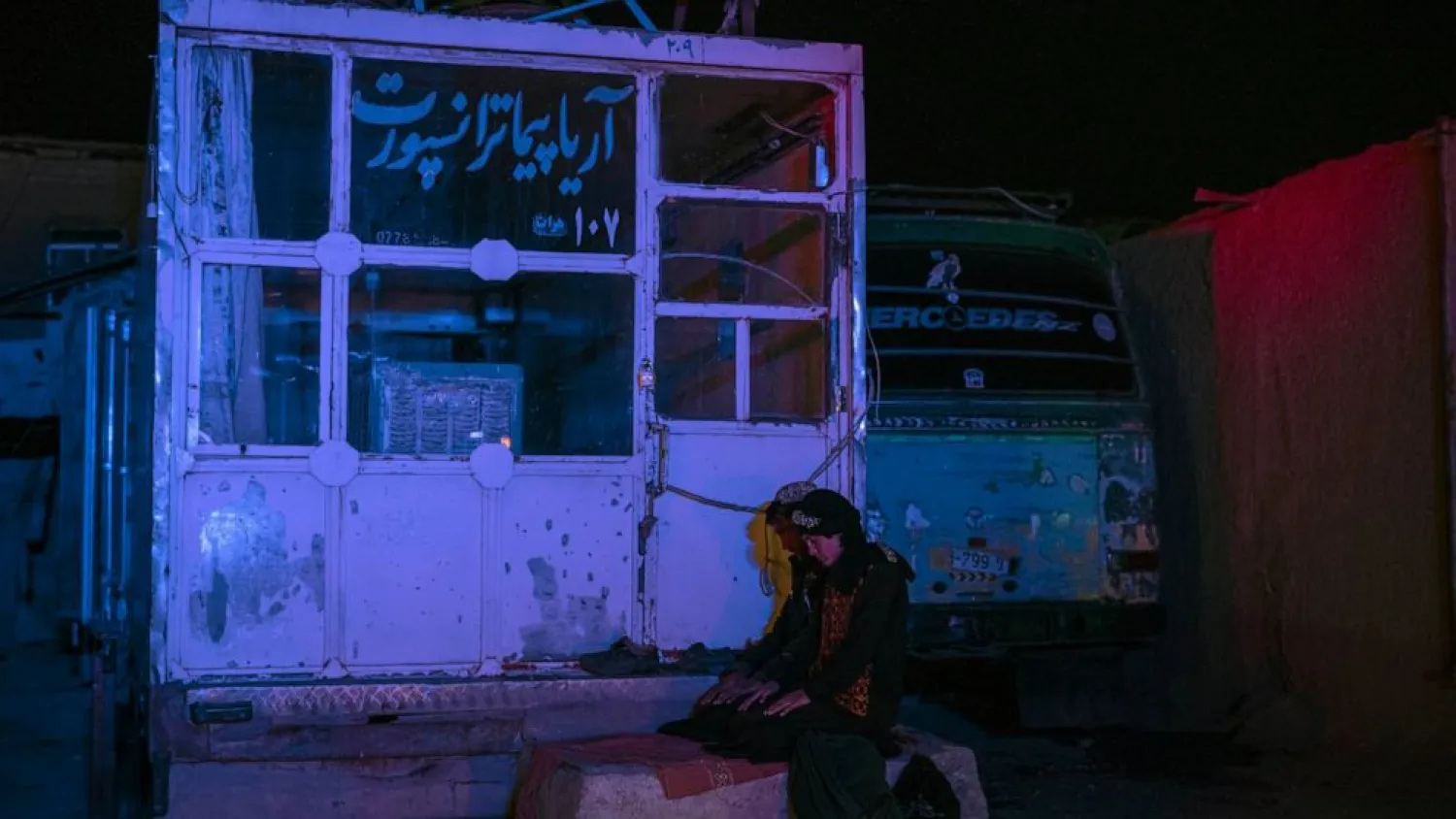 Two Afghan men pray at a bus station in Herat, Afghanistan, on Tuesday, Nov. 23, 2021, before they embark on a bus for a 300-mile trip south to Nimrooz near the Iranian border. (AP Photo/Petros Giannakouris)