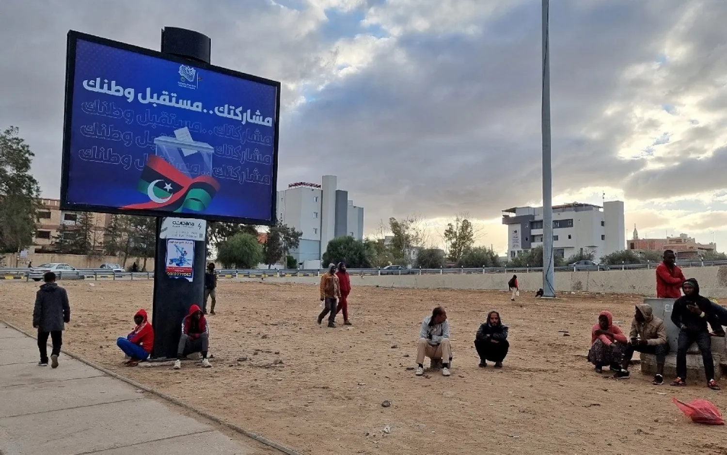 Workers sit near an electoral billboard reading in Arabic "your participation is the future of your country" in Libya's capital Tripoli. (AFP)