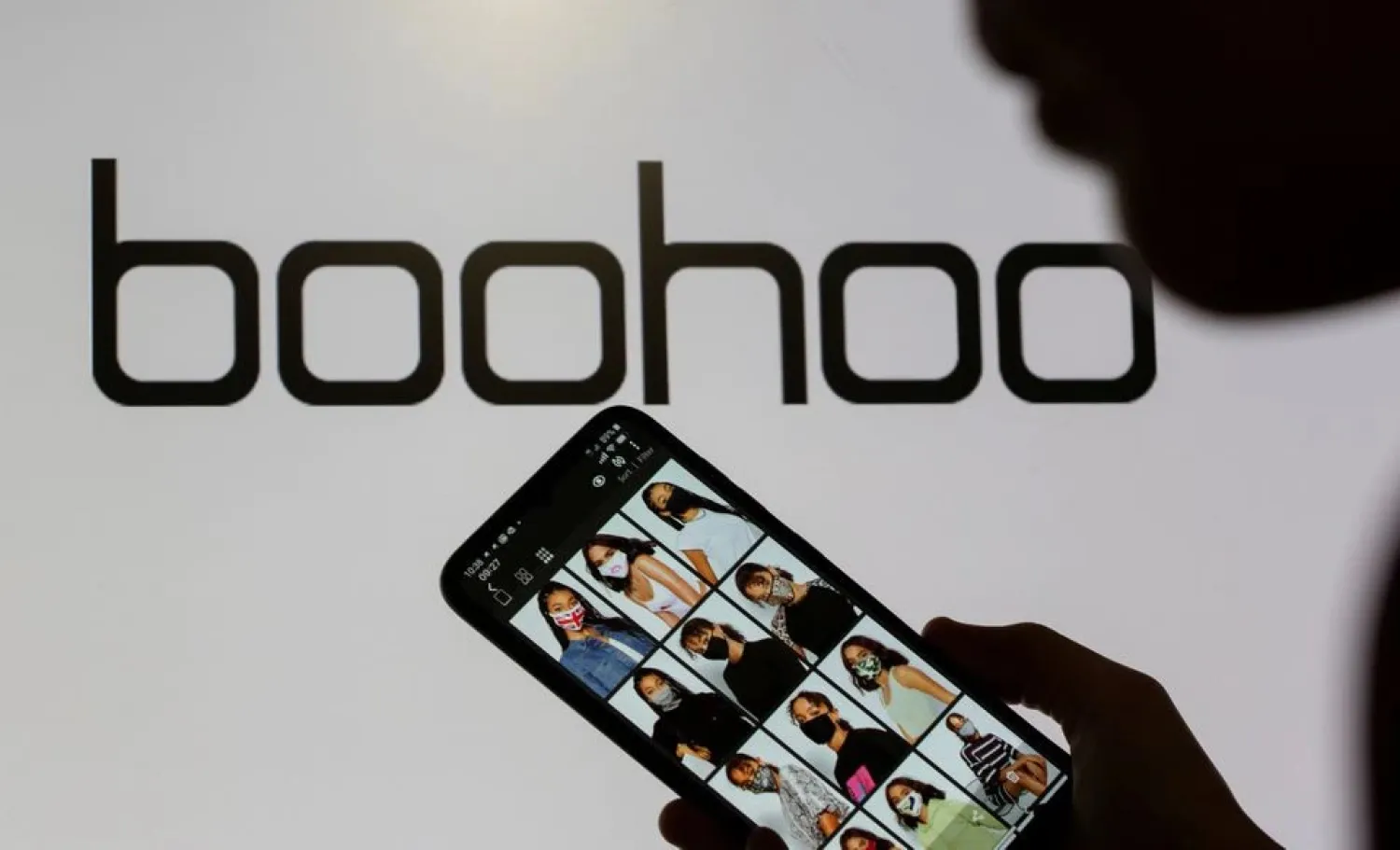 A woman poses with a smartphone showing the Boohoo app in front of the Boohoo logo on display in this illustration taken September 30, 2020. REUTERS/Dado Ruvic/Illustration/File Photo


