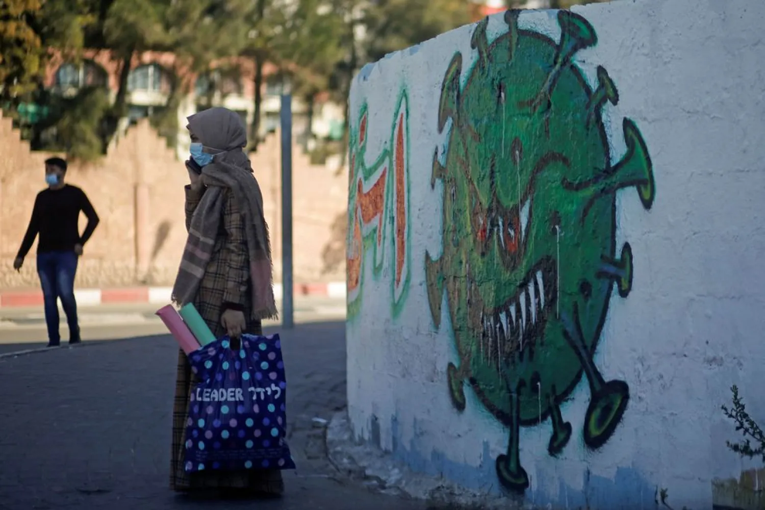 A Palestinian woman wearing on a protective face mask speaks on her phone as she stands next to a coronavirus-themed mural amid the coronavirus disease (COVID-19) outbreak, in Gaza City November 22, 2020. REUTERS/Mohammed Salem

