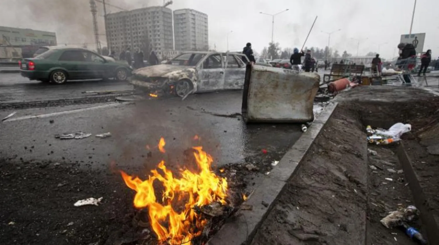 People walk past cars, which were burned after clashes, on a street in Almaty, Kazakhstan, Friday, Jan. 7, 2022. (AP Photo/Vasily Krestyaninov)