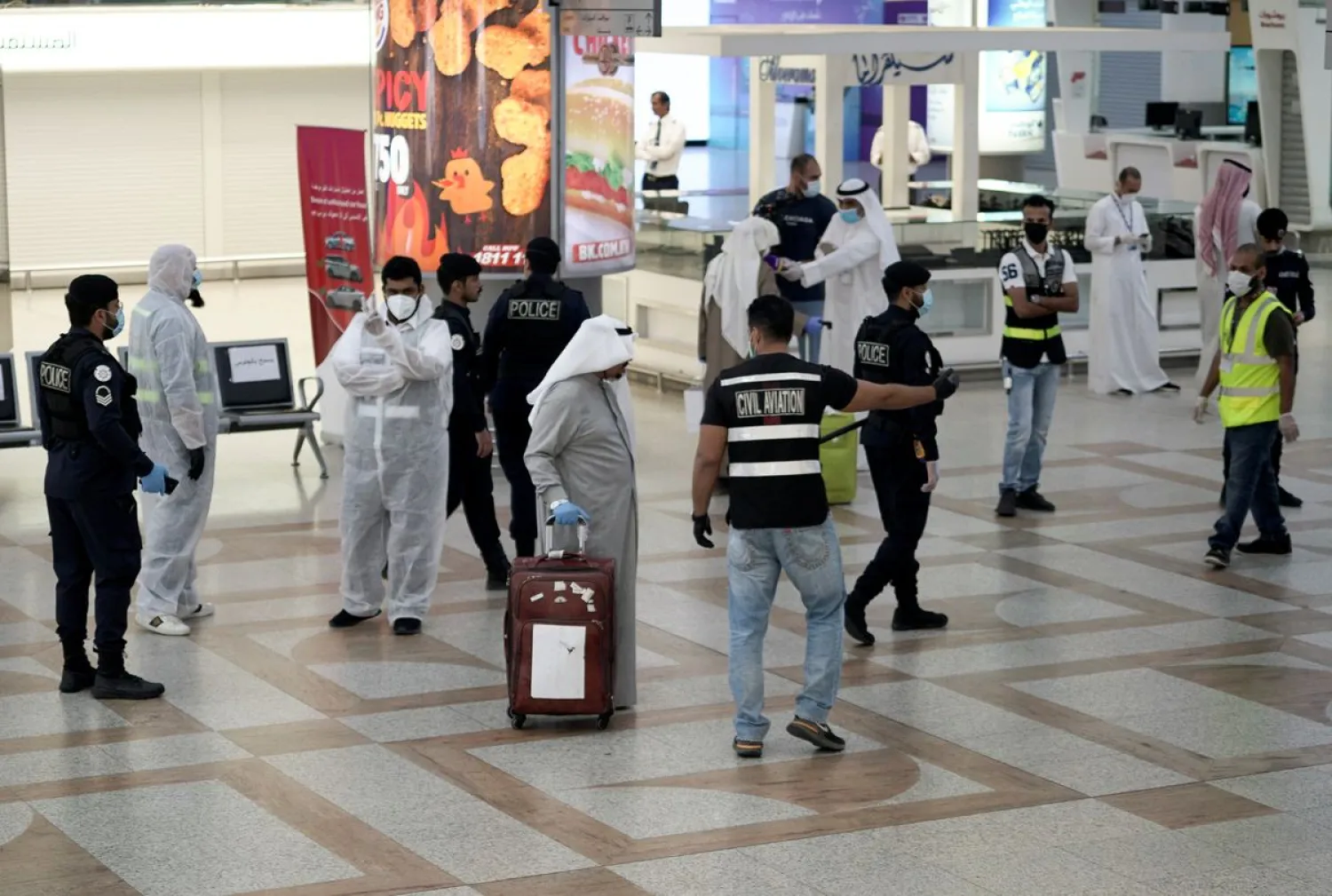 A Kuwaiti passenger holding his luggage walks by the police and civil aviation personnel upon his arrival from Amman at Kuwait Airport, following the outbreak of the coronavirus disease (COVID-19), in Kuwait City, Kuwait April 21, 2020. Reuters