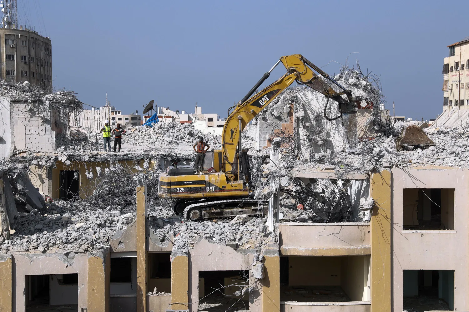 Palestinian workers use a backhoe to break and remove parts of the Al-Jawhara building, that was damaged in Israeli airstrikes during Israel's war with Gaza's Hamas rulers last May, in the central al-Rimal neighborhood of Gaza City, Nov. 16, 2021. (AP Photo/Adel Hana)
