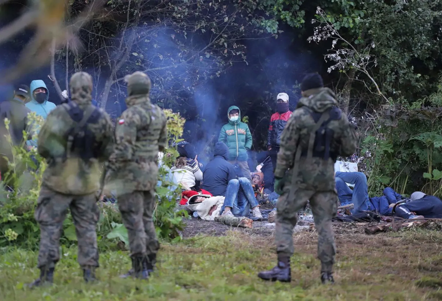 Polish border patrol officers guard a group of migrants who attempted to cross the border between Belarus and Poland near the village of Usnarz Gorny, Poland August 18, 2021. Grzegorz Dabrowski/Agencja Gazeta/via REUTERS