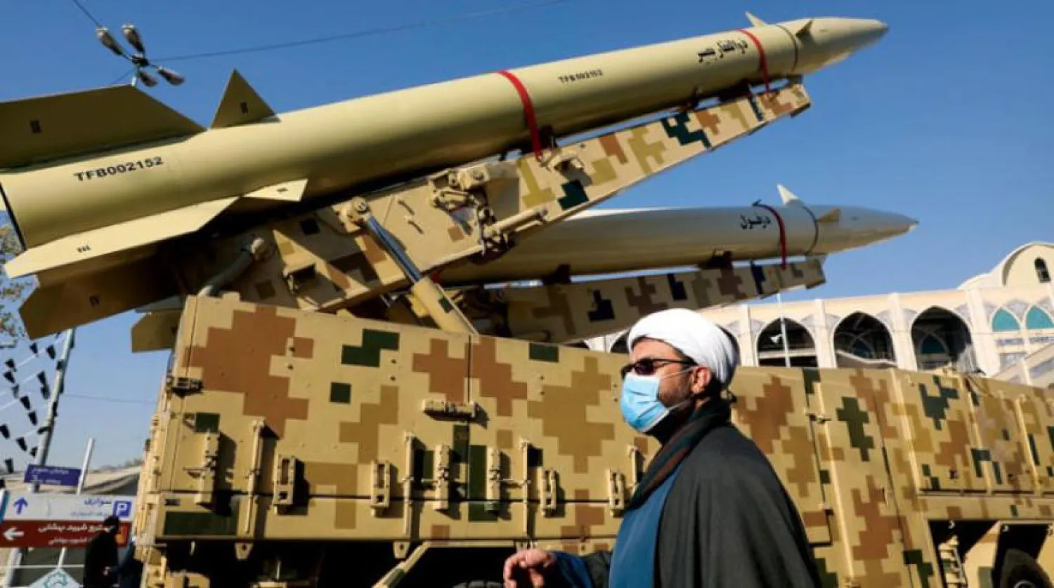 Bu ay Tahran'da düzenlenen DMO sergisinde füzelerin yakınından geçen bir din adamı (AP)