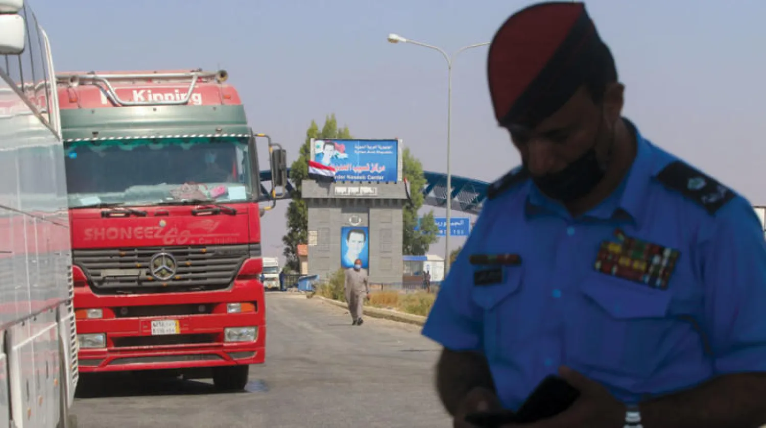 ضابط أردني يتفقد هاتفه بينما يصطف المسافرون والشاحنات في طابور لدخول الأردن عند معبر جابر في 29 سبتمبر الماضي (غيتي)