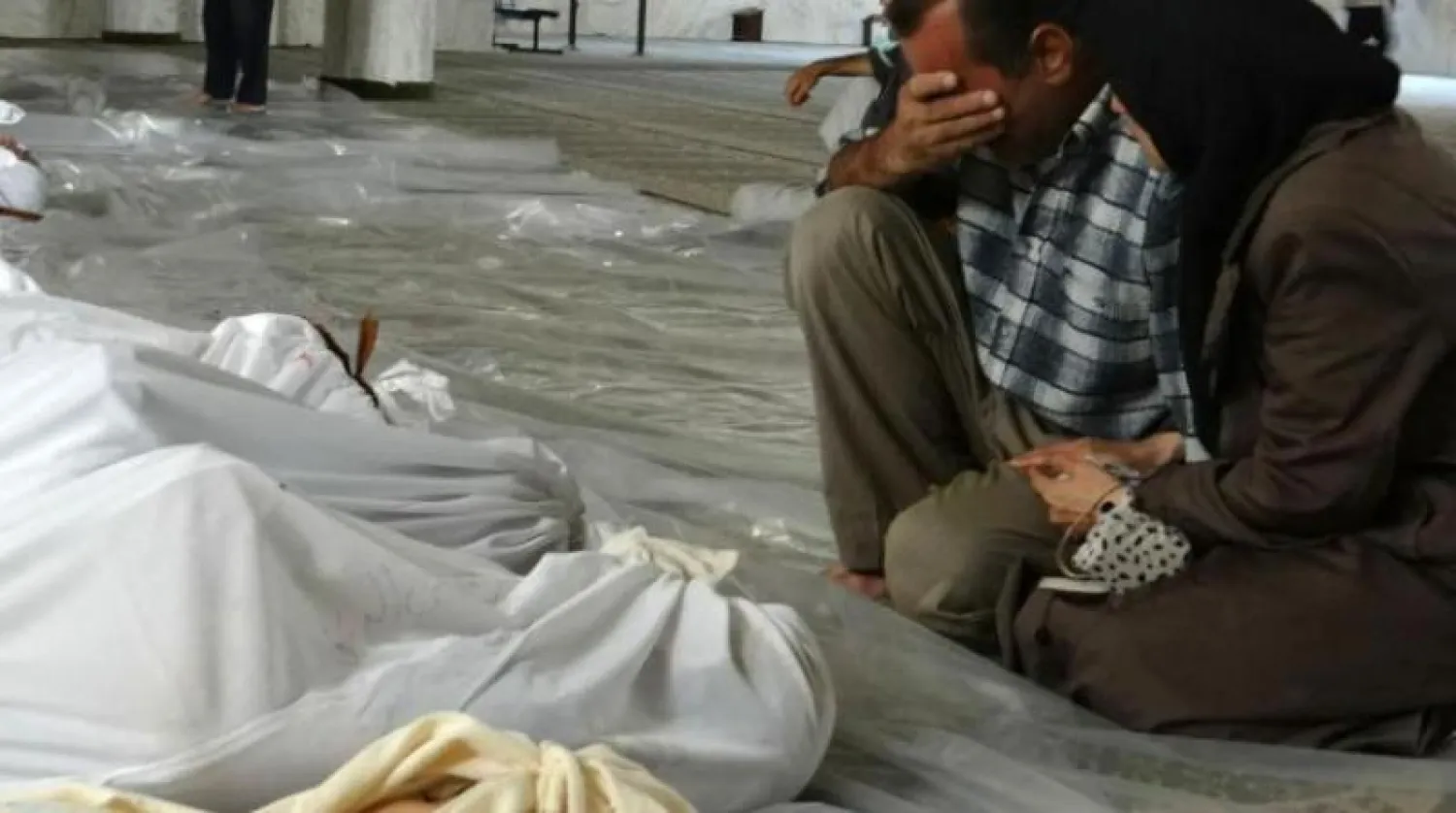 زوجان سوريان يبكيان أمام جثث ملفوفة في أكفان عقب هجوم بالغاز السام (أرشيفية - أ.ف.ب)