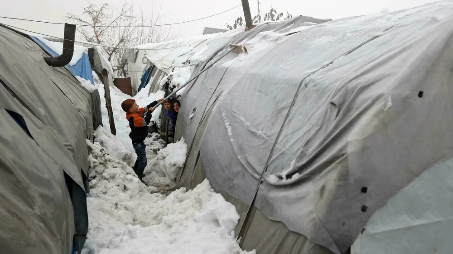 A boy clears snow from one of the tents at a camp for the internally displaced near the city of Jisr al-Shughur in Syria's northwestern province of Idlib on January 26, 2022. (AFP)
