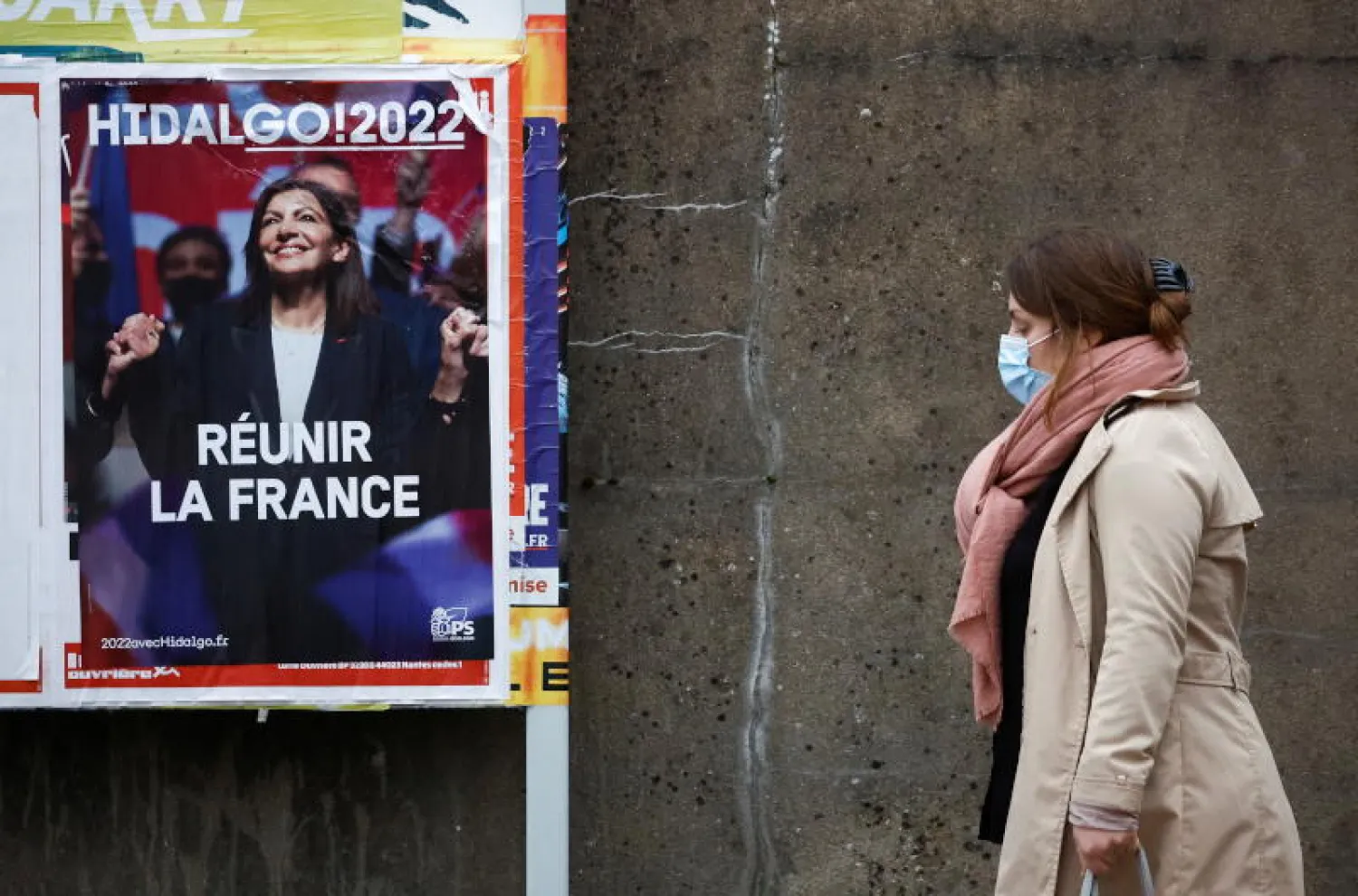 سيدة تضع كمامة تمر في أحد شوارع نانت قرب لوحة دعائية لآن هيدالغو المرشحة الاشتراكية للرئاسة الفرنسية (أ ف ب)
