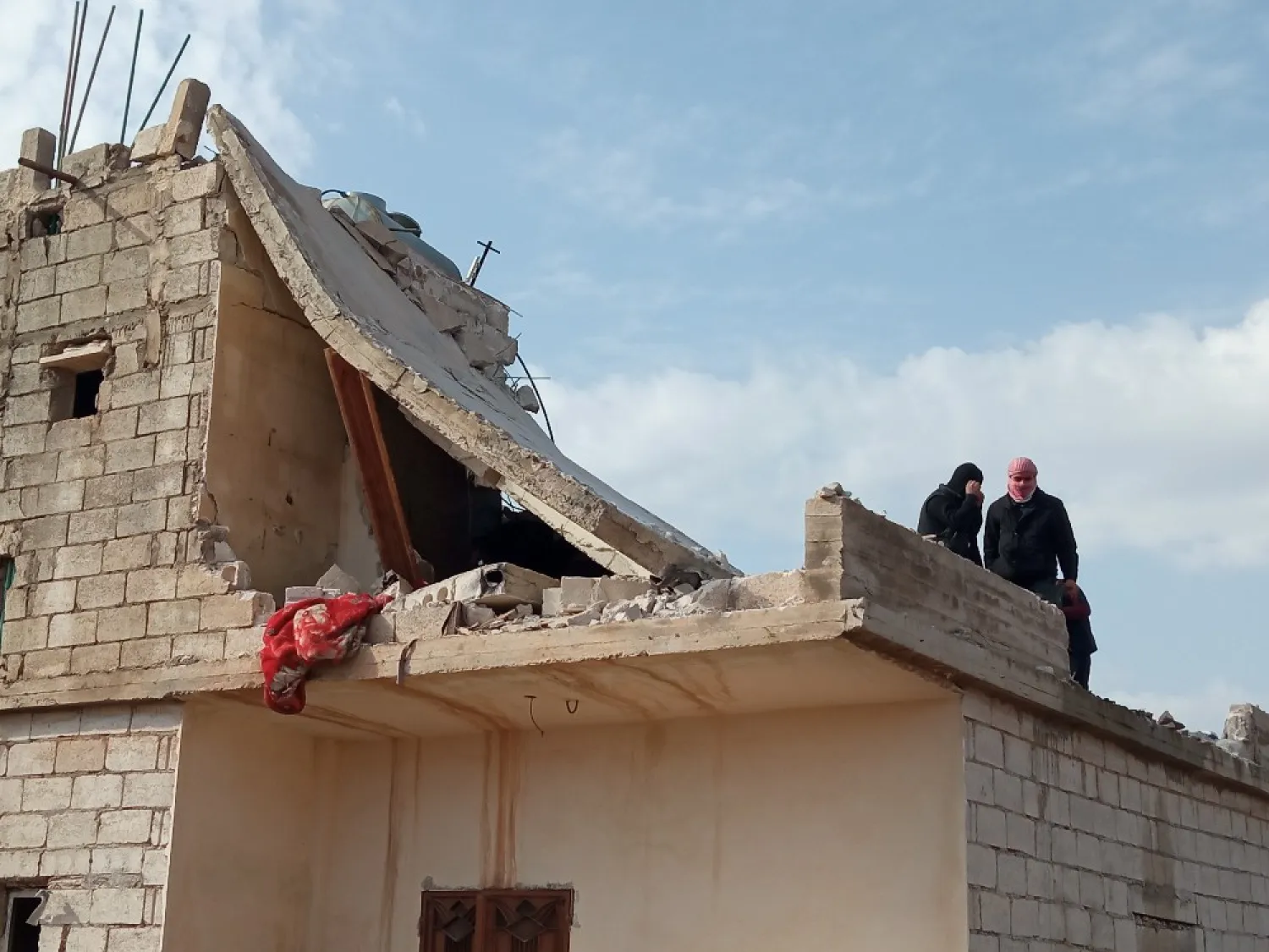 شخصان يقفان فوق سطح أحد المنازل المتضررة (الشرق الأوسط)