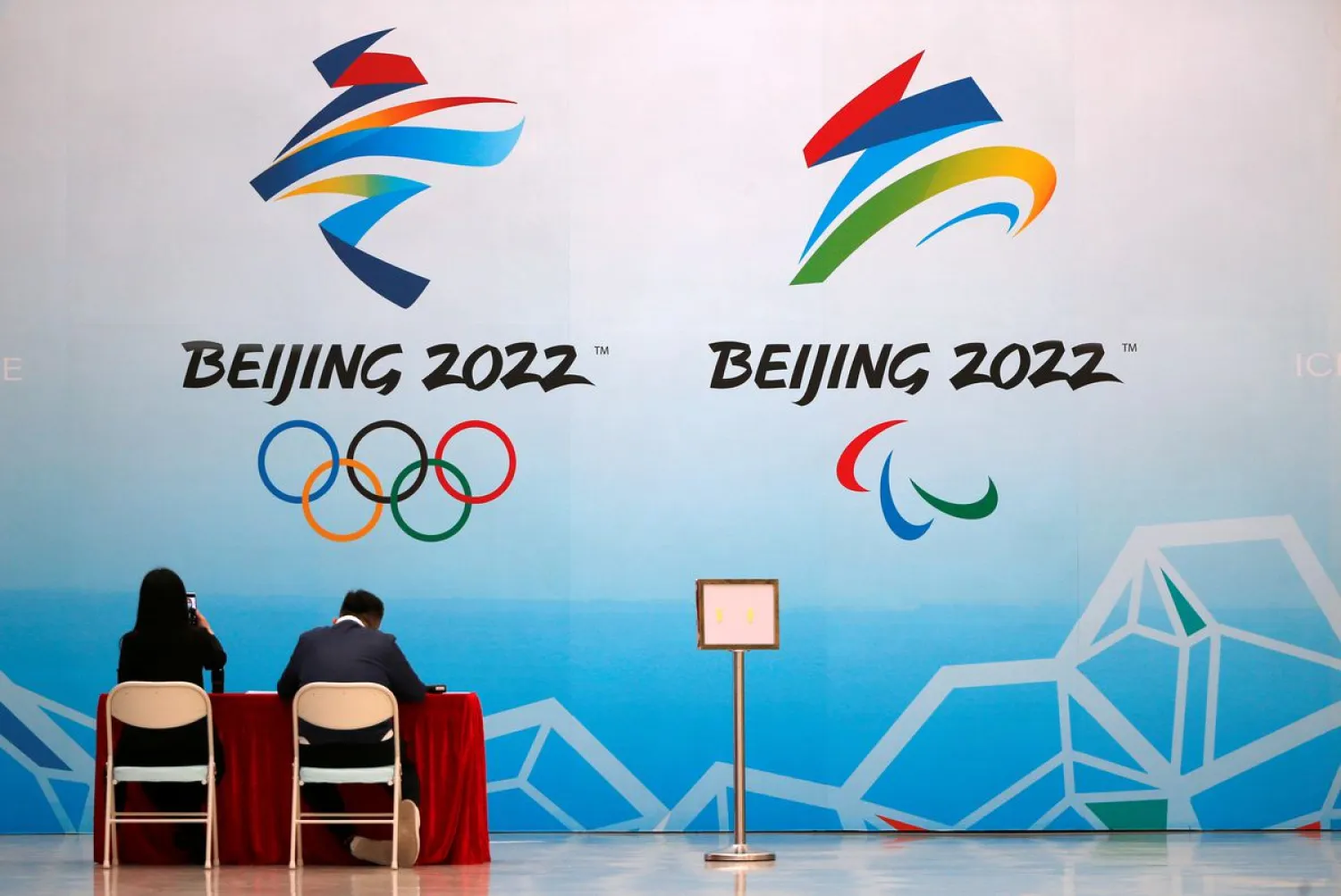 Staff members sit near a board with signs of the 2022 Olympic Winter Games. Reuters