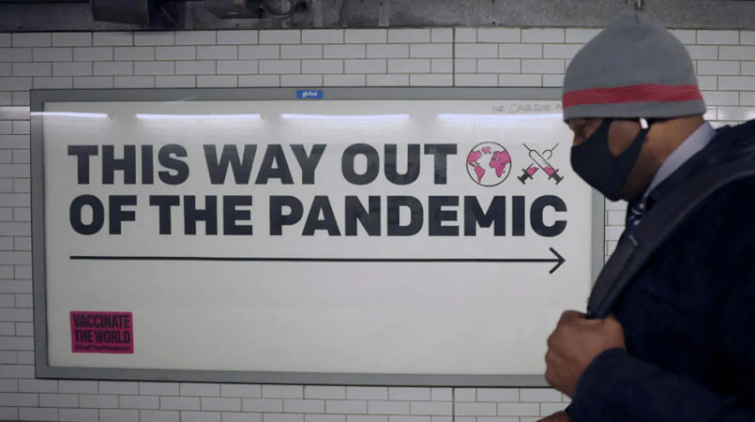 لافتة تحث على توسيع حملات التلقيح ضد كورونا في محطة قطار بلندن (رويترز)