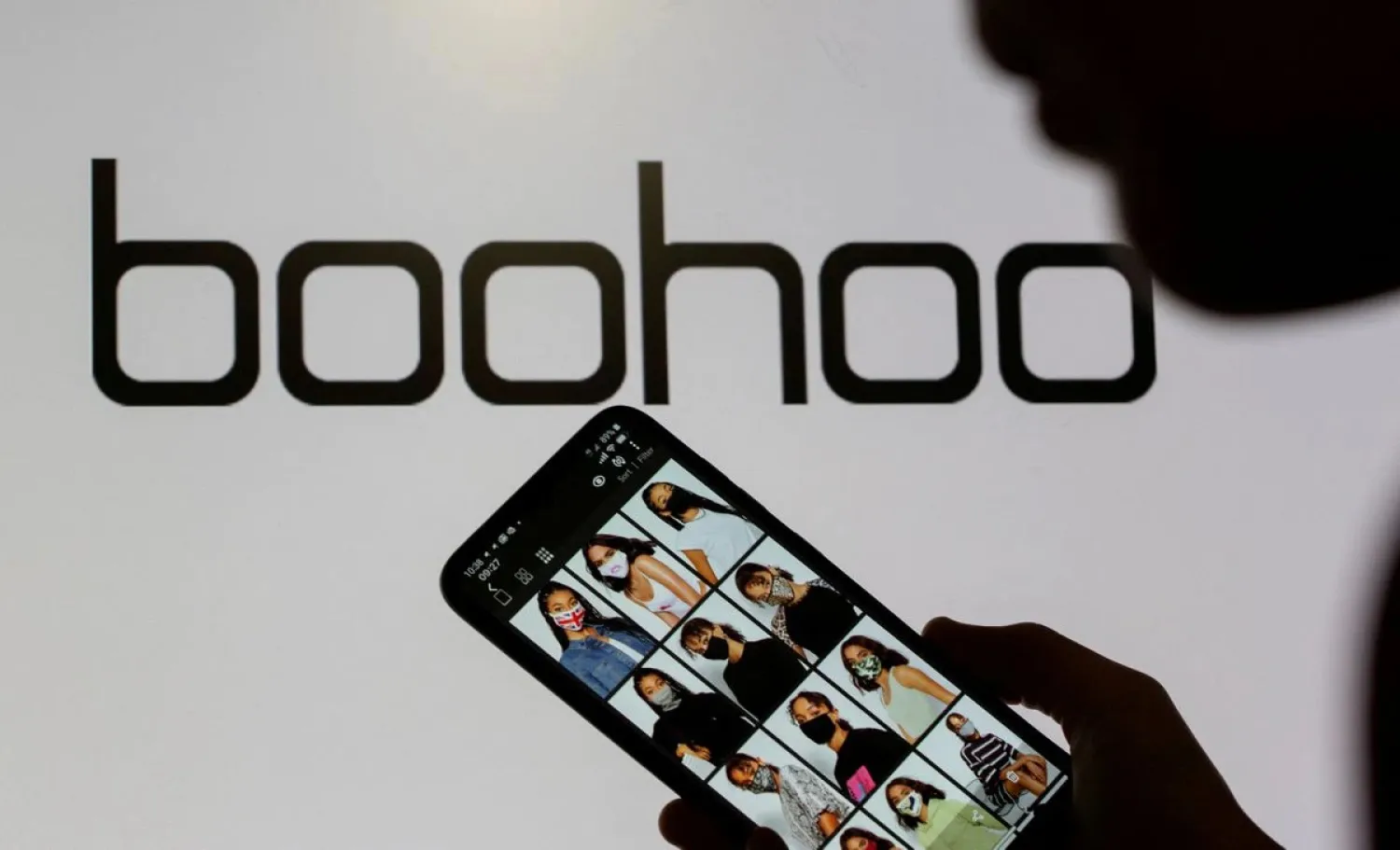A woman poses with a smartphone showing the Boohoo app in front of the Boohoo logo on display in this illustration taken September 30, 2020. (Reuters)