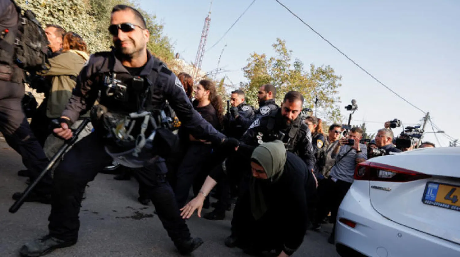 عنصر من قوات الأمن الإسرائيلية يعتدي على سيدة فلسطينية خلال مظاهرة في حي الشيخ جراح أمس (رويترز)