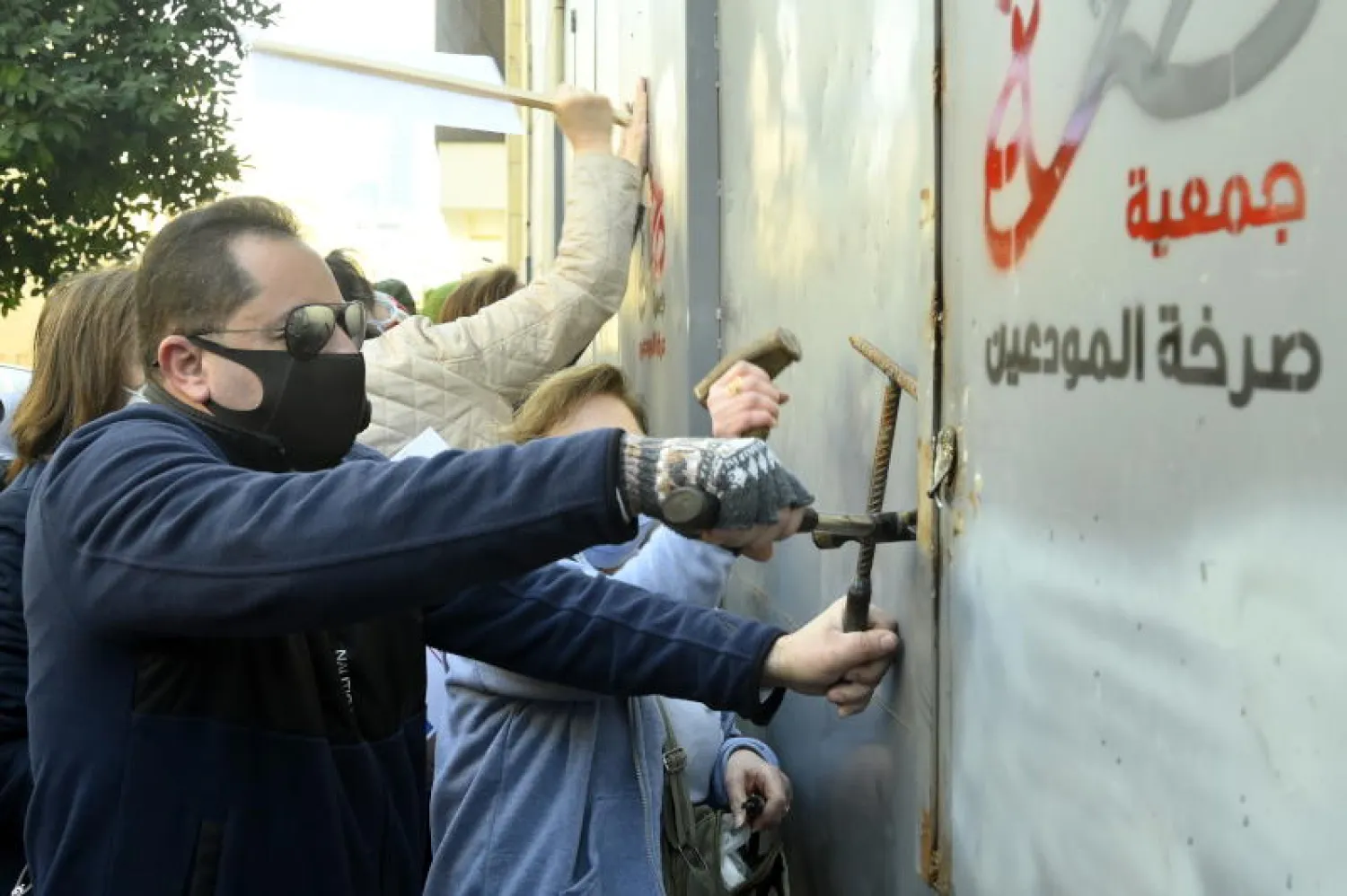 عملاء بنك يحاولون فتح باب أحد البنوك خلال مظاهرة في بيروت أول أمس للسماح لهم بسحب ودائعهم (إ.ب.أ)