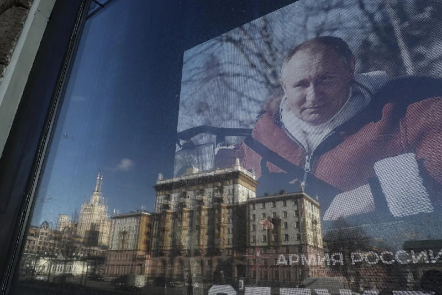 صورة للسفارة الأميركية منعكسة في نافذة متجر يعرض صورة للرئيس الروسي فلاديمير بوتين في العاصمة الروسية موسكو (إ.ب.أ)