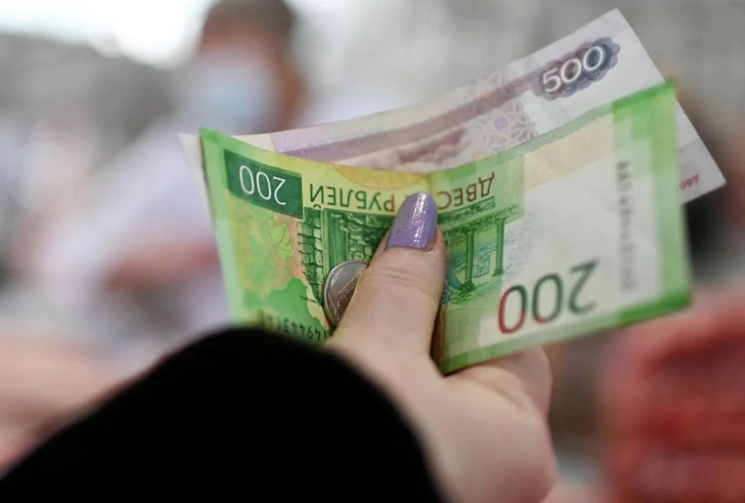 A customer hands over Russian rouble banknotes and coins to a vendor at a market in Omsk, Russia February 18, 2022. (Reuters)