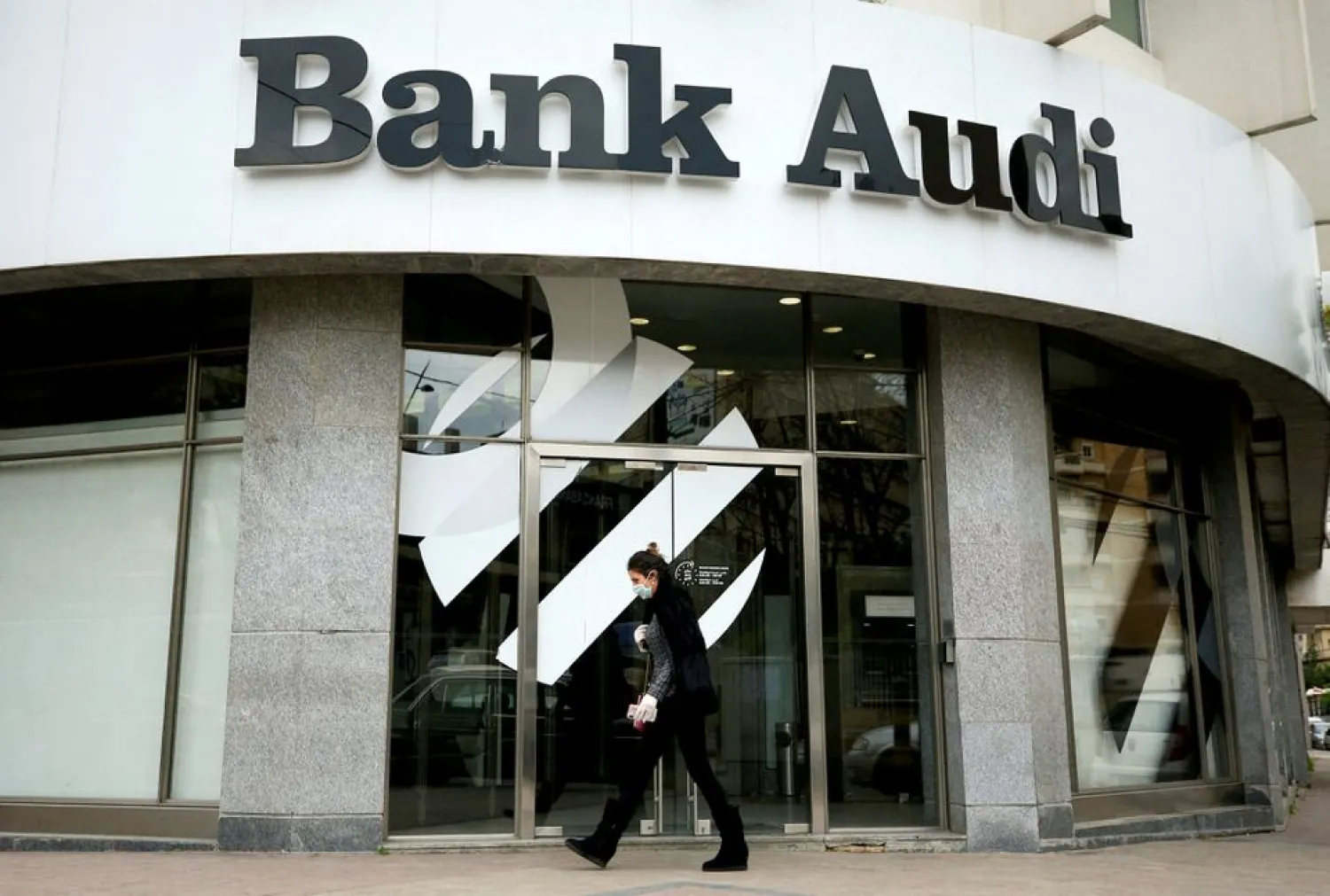 A woman wearing a face mask walks by a closed branch of Bank Audi after Lebanon declared a state of emergency over the spread of the coronavirus, in Sidon, Lebanon, March 17, 2020. (Reuters)