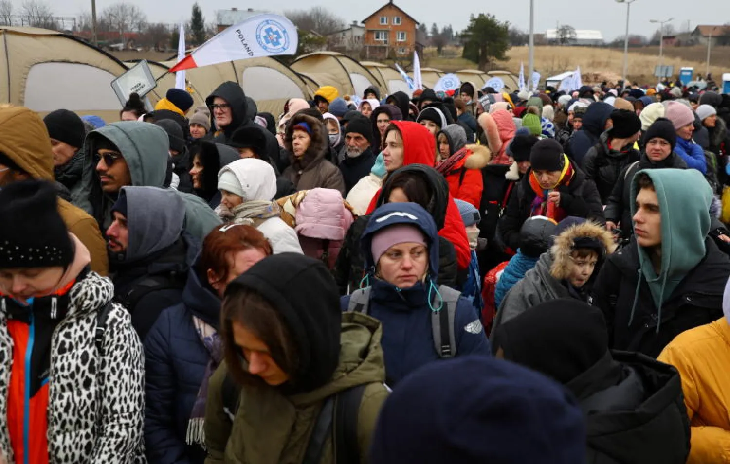 أوكرانيون ينتظرون ركوب حافلة بعد عبورهم الحدود من أوكرانيا إلى بولندا عند نقطة التفتيش الحدودية في ميديكا (رويترز)