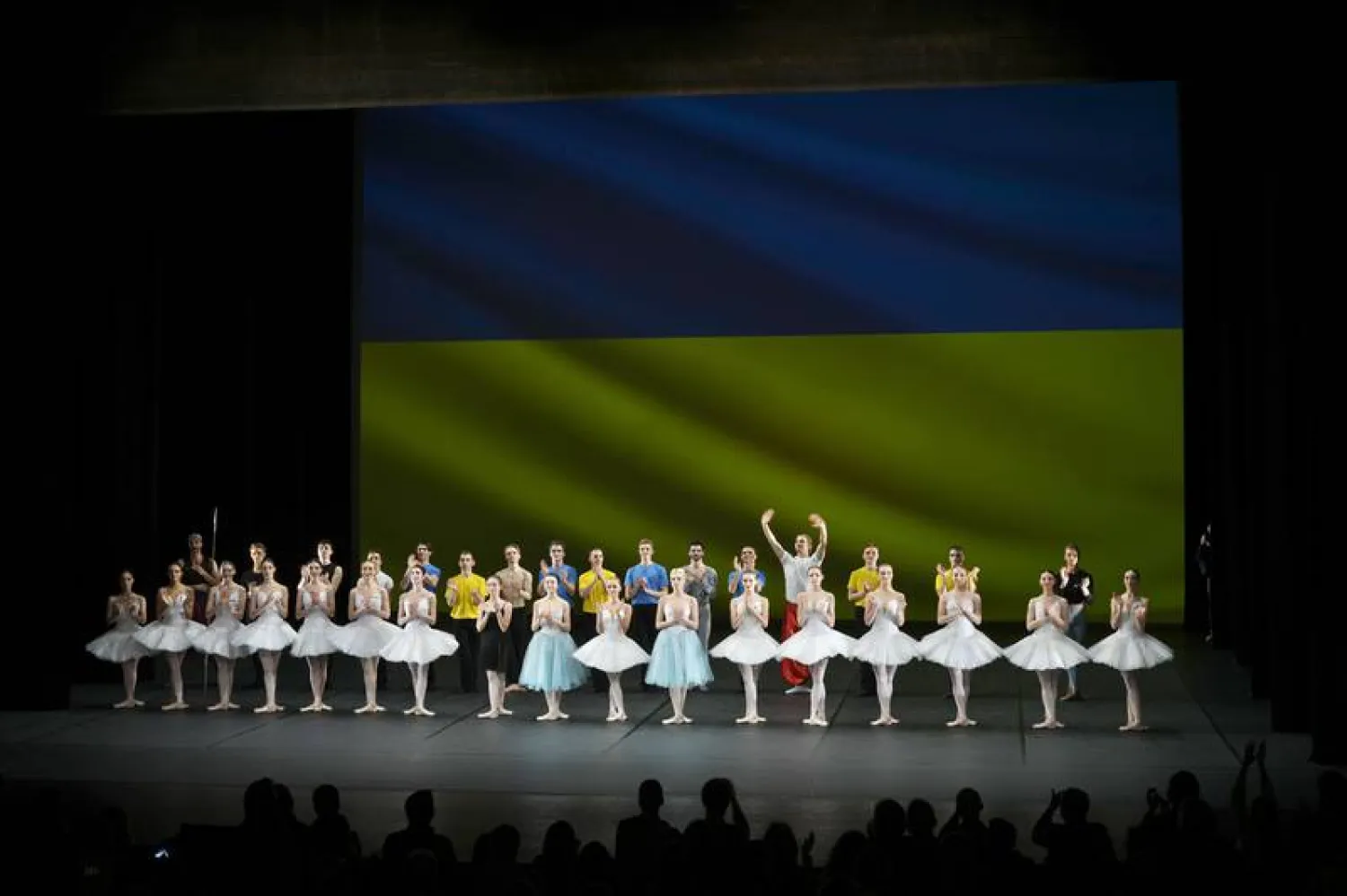 Ukrainian dancers of the Kyiv City Ballet company acknowledge applause in front of Ukrainian flag projected onto a screen at the end of a performance, at the Theatre de Chatelet, in Paris, Tuesday, March 8, 2022. (AP Photo/Thibault Camus)