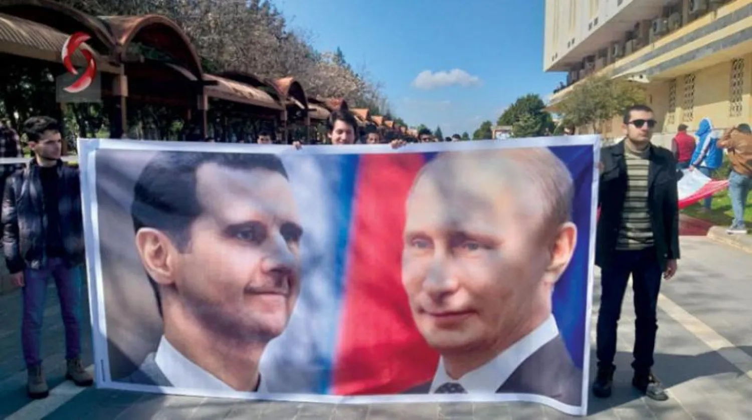 Students are forced to raise a poster in support of Assad and Putin at the Baath University in Homs, Syria. (Social media)