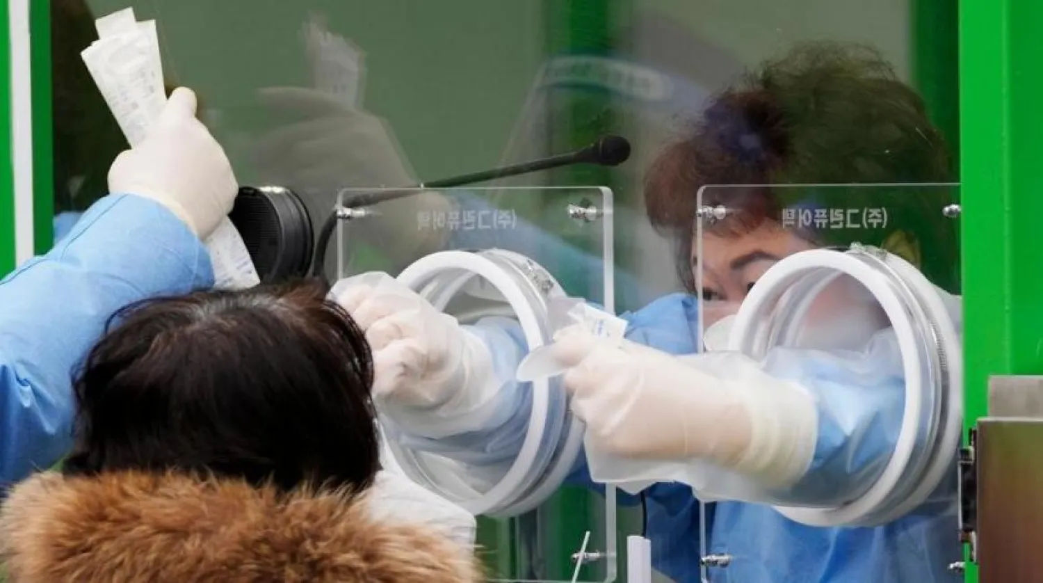 A medical worker wearing protective gear in a booth takes a sample from a woman at a temporary screening clinic for the coronavirus in Seoul, South Korea, Friday, Dec. 10, 2021. (AP Photo/Lee Jin-man)
