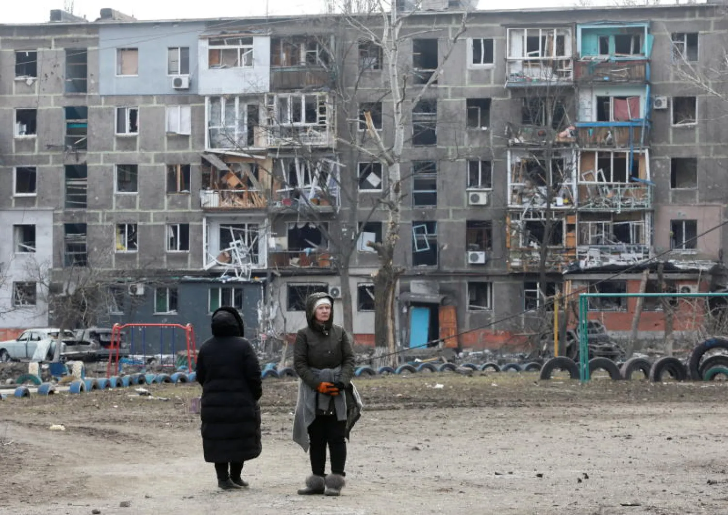 سيدتان تقفان أمام مبنى سكني دمره القصف في مدينة ماريوبول الأوكرانية (رويترز)