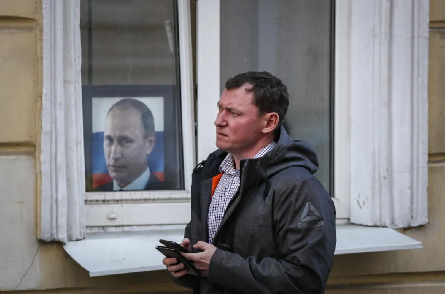 روسي يسير بجانب ملصق للرئيس فلاديمير بوتين خلف نافذة أحد المباني في موسكو(إ.ب.أ)