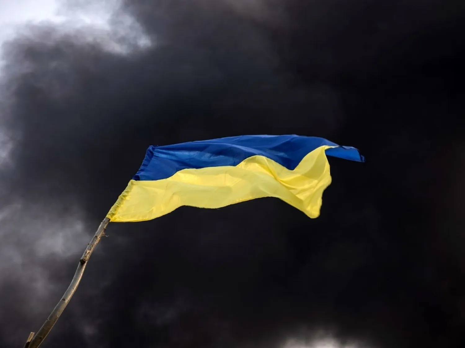 Smoke rises behind a Ukrainian flag after Russian attacks hit a fuel storage facility in the city of Kalynivka. FADEL SENNA AFP

