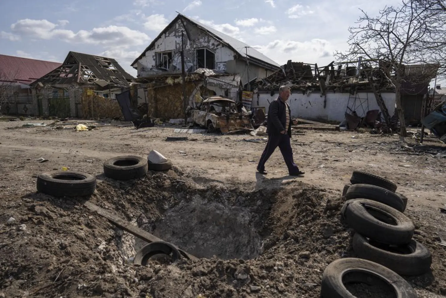 A man walks behind a crater created by a bomb and in front of damaged houses following a Russian bombing earlier this week, outskirts Mykolaiv, Ukraine, Friday, 25, 2022.(AP)