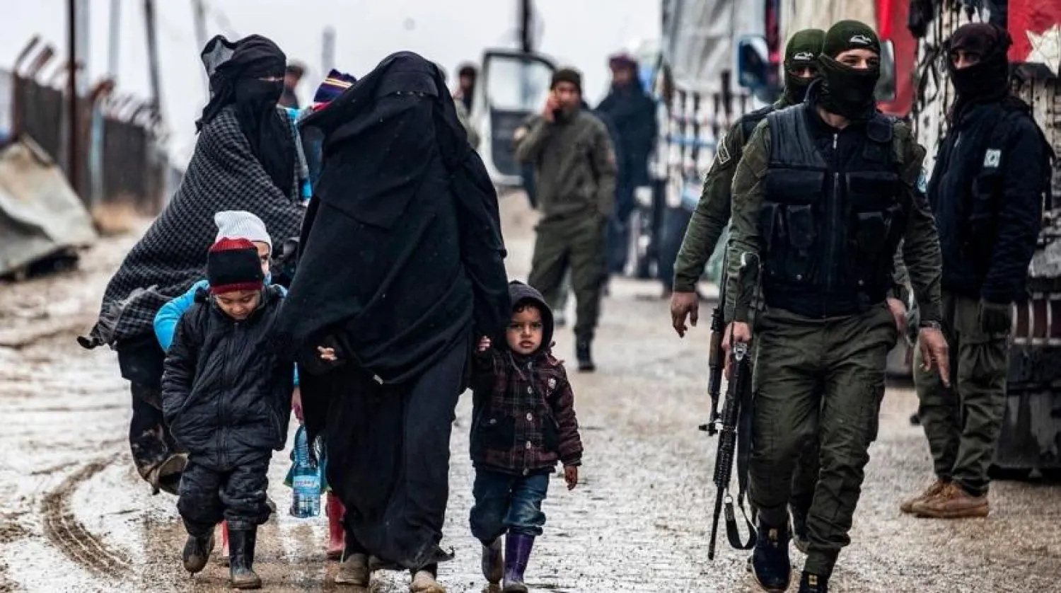 A veiled woman walks with children next to a member of the Syrian Kurdish internal security services known as Asayish at al-Hol camp in Hasakah governorate in northeastern Syria, on January 19, 2021. (Delil Souleiman/AFP)
