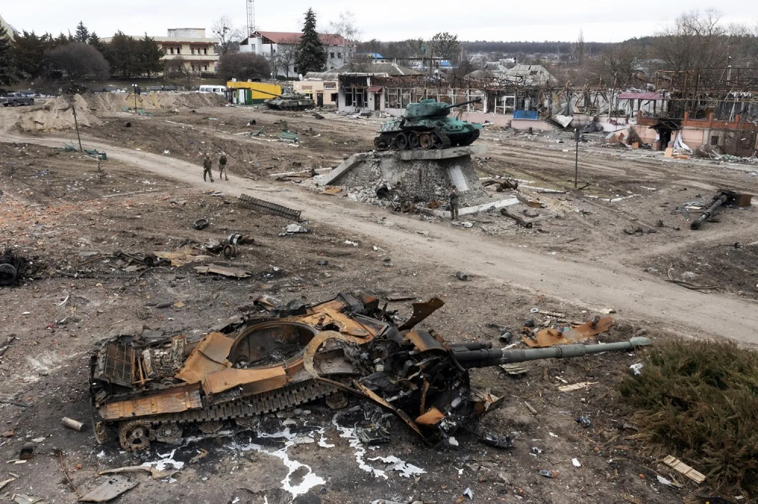 Local residents pass by a damaged Russian tank in the town of Trostyanets, east of capital Kyiv, Ukraine, Monday, March 28, 2022. The monument to Second World War is seen in background. (AP)