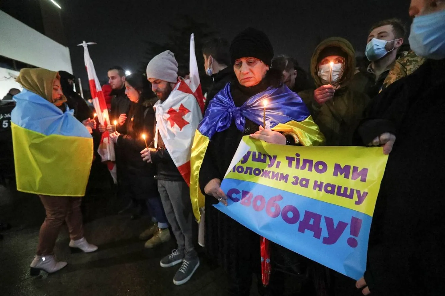 People attend a ceremony to pay tribute to fallen Georgian military volunteers Gia Beriashvili and Davit Ratiani, who joined Ukrainian armed forces, were killed during Ukraine-Russia conflict and were repatriated to homeland, at an airport in Tbilisi, Georgia, March 24, 2022. A placard reads: "We'll lay down soul, body for our freedom!" (Reuters)