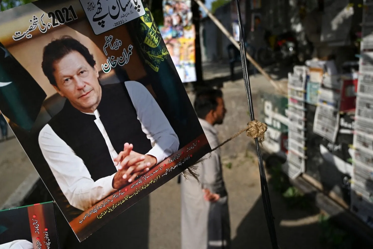 A resident stands beside a picture of Pakistan's Prime Minister Imran Khan as he looks at the morning newspapers displayed for sale at a roadside stall in Islamabad, Pakistan, April 4, 2022. (AFP)