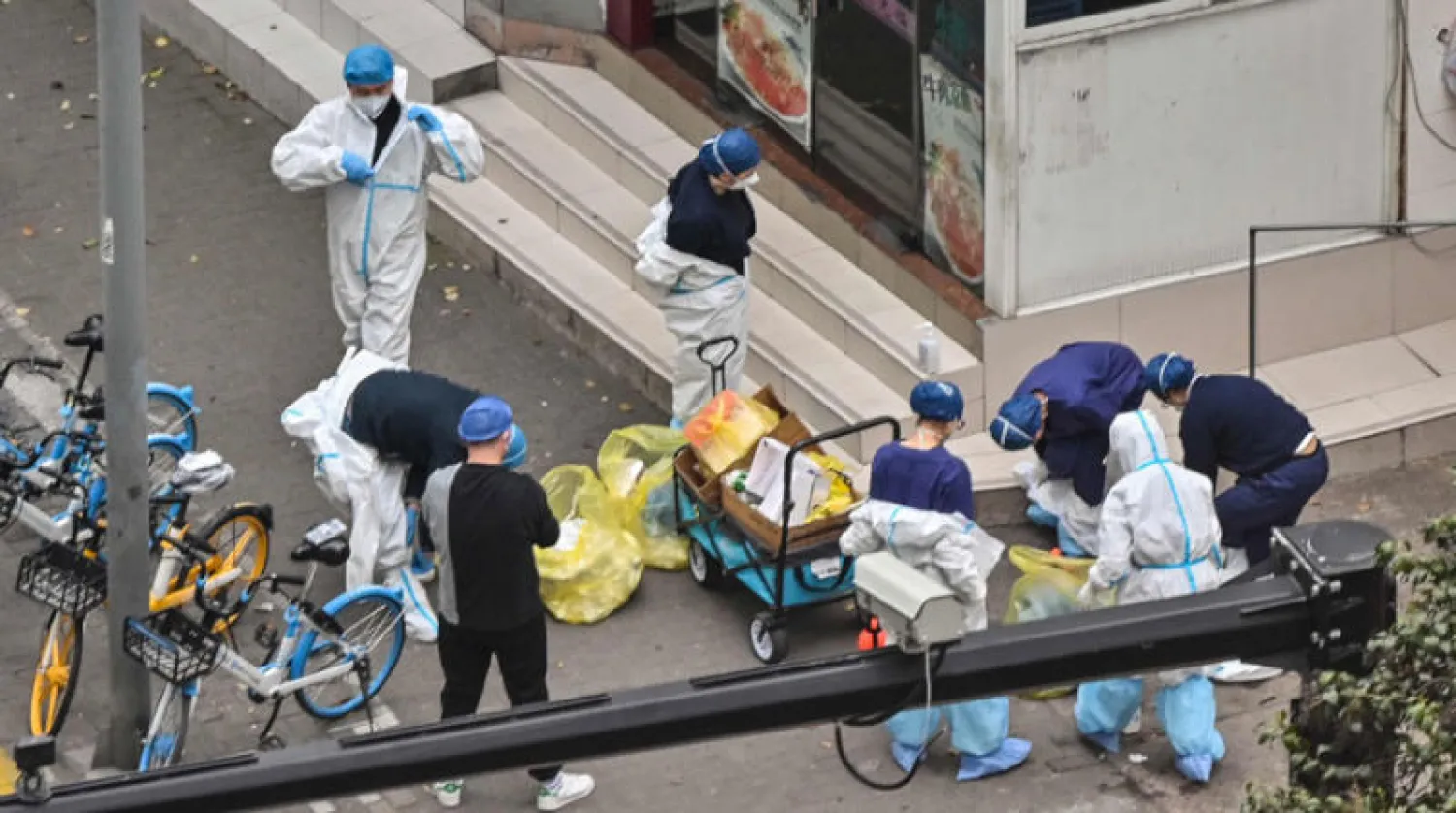 عمال يخلعون ملابسهم الواقية بجوار مدخل أحد الأحياء المغلقة في شنغهاي أمس (أ.ف.ب)