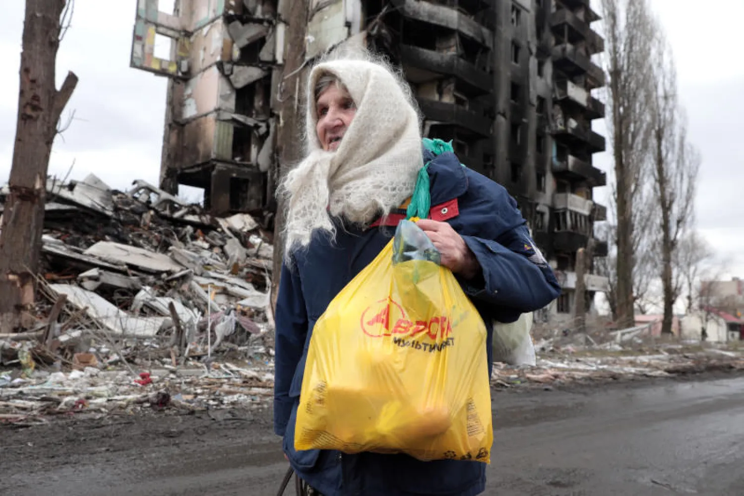 امرأة مسنة تسير مقابل مبنى دمره القصف الروسي في محيط كييف (د.ب.أ)