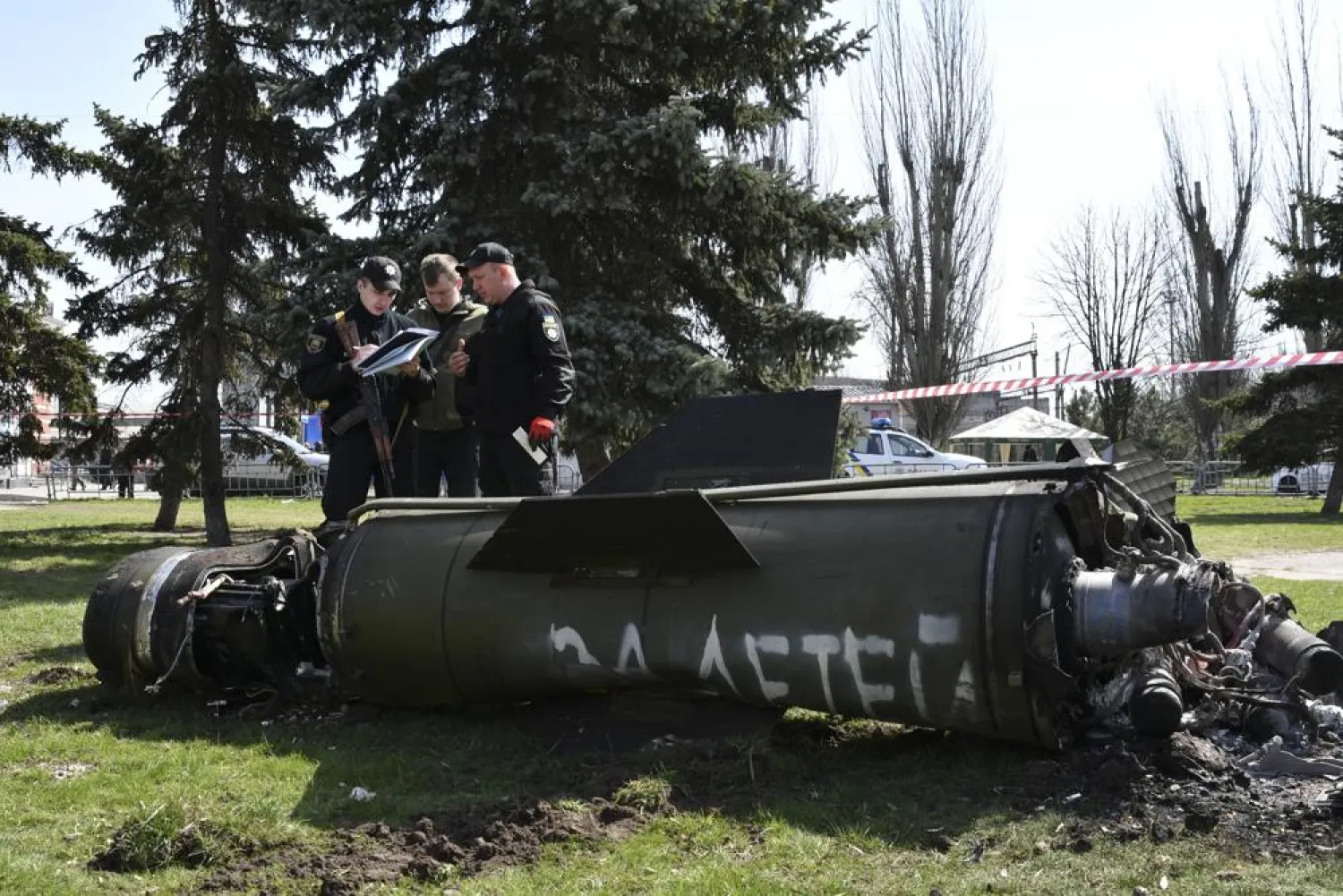 Ukrainian servicemen stand next to a fragment of a Tochka-U missile with a writing in Russian "For children" , on a grass after Russian shelling at the railway station in Kramatorsk, Ukraine, Friday, April 8, 2022. (AP)