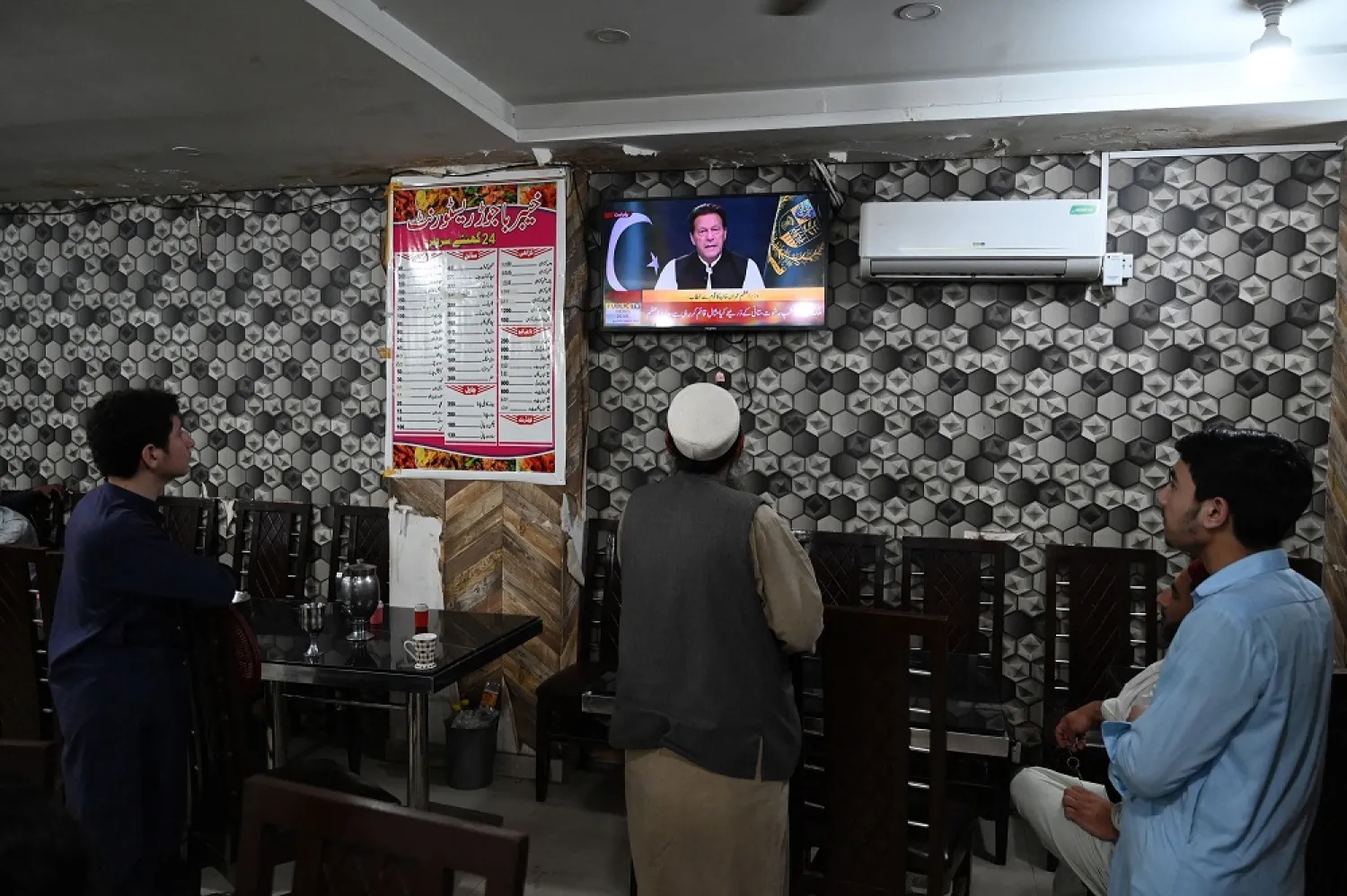 People listen to Pakistan's Prime Minister Imran Khan addressing the nation on television at a restaurant in Islamabad on April 8, 2022. (AFP)