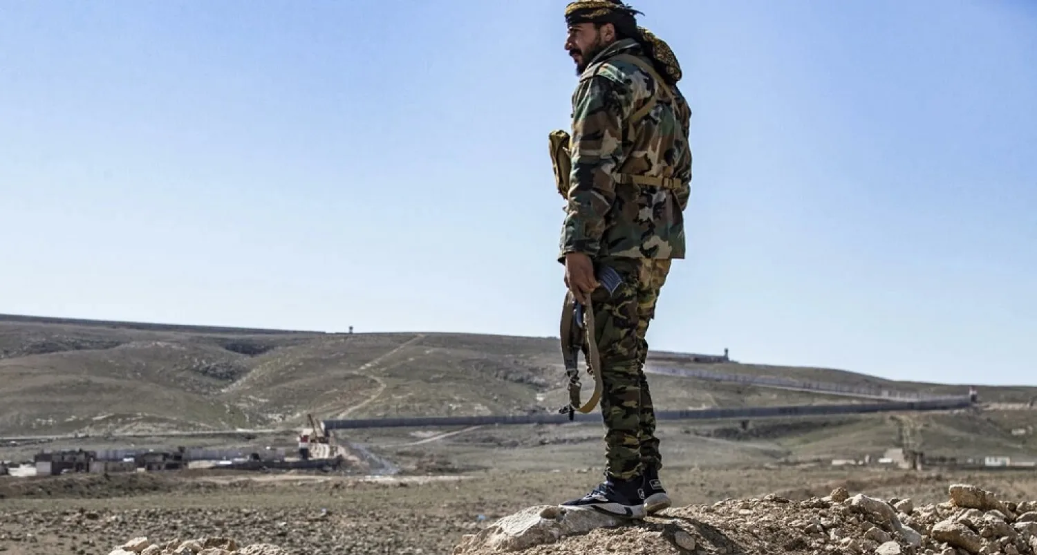 A member of the border guard force loyal to the Syrian Democratic Forces (SDF) looks on near Syria's town of Al-Hol at ongoing construction of a concrete border fence being erected on the Iraqi side. (AFP)
