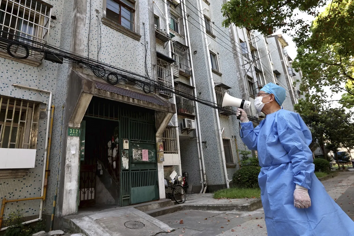 In this photo released by China's Xinhua News Agency, a volunteer uses a megaphone to talk to residents at an apartment building in Shanghai, China, Tuesday, April 12, 2022. (AP)
