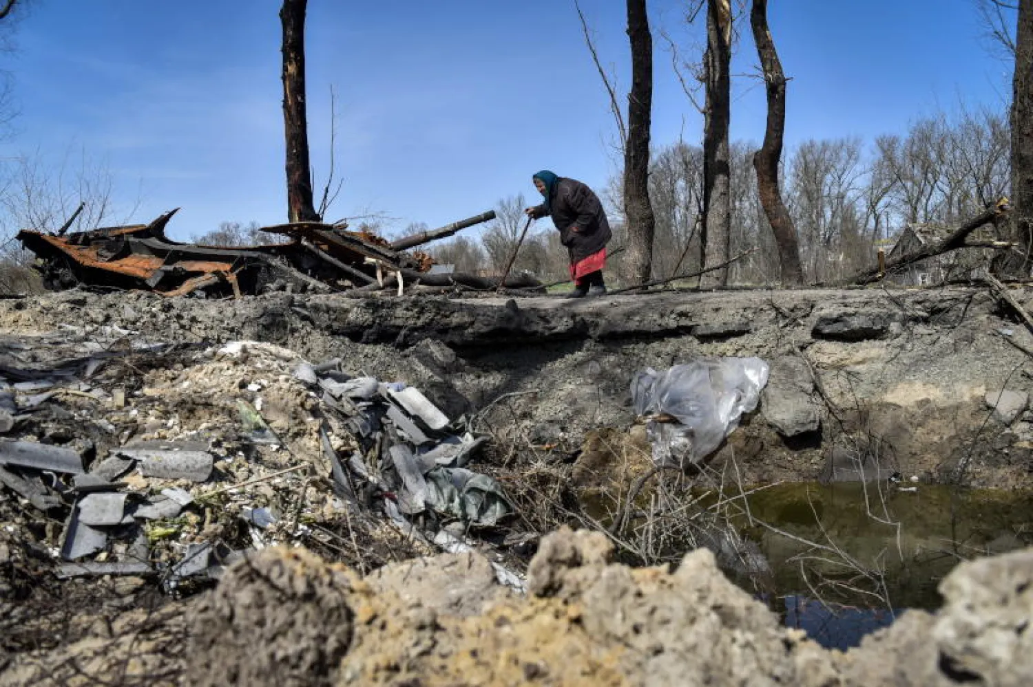 سيدة تمر بجانب حفرة خلفها انفجار قنبلة جوية على طريق في شمال كييف (إ.ب.أ)