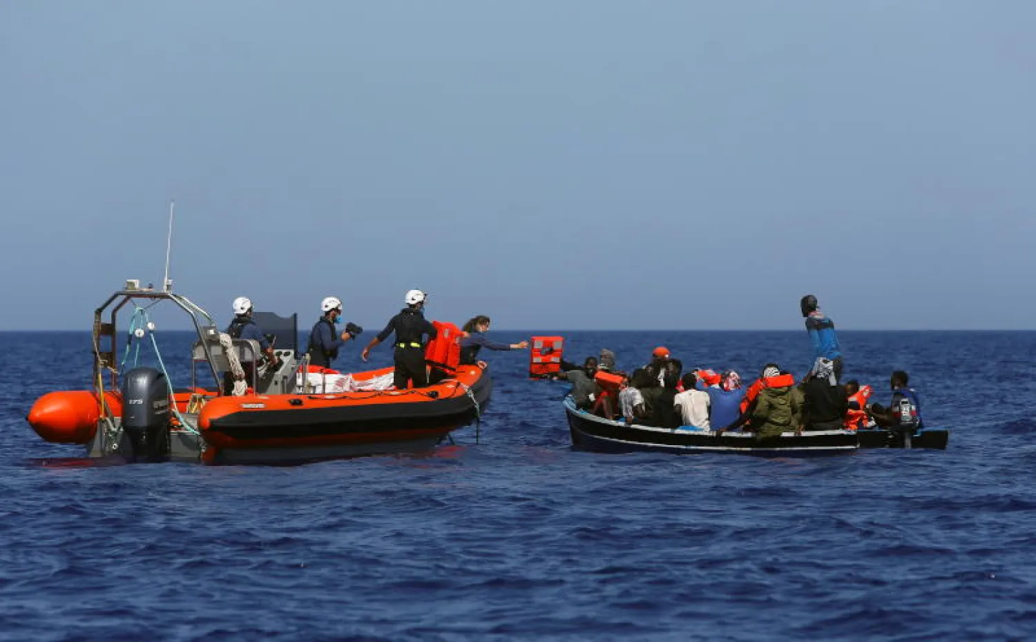 طاقم سفينة إنقاذ يساعد مهاجرين في قارب خشبي صغير قبالة سواحل ليبيا (رويترز)