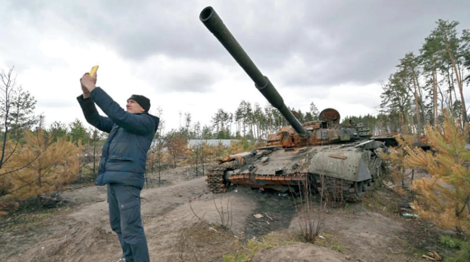 أحد سكان ضواحي كييف يعود إلى منطقته ويأخذ صورة «سيلفي» أمام دبابة روسية محطمة (أ.ف.ب)