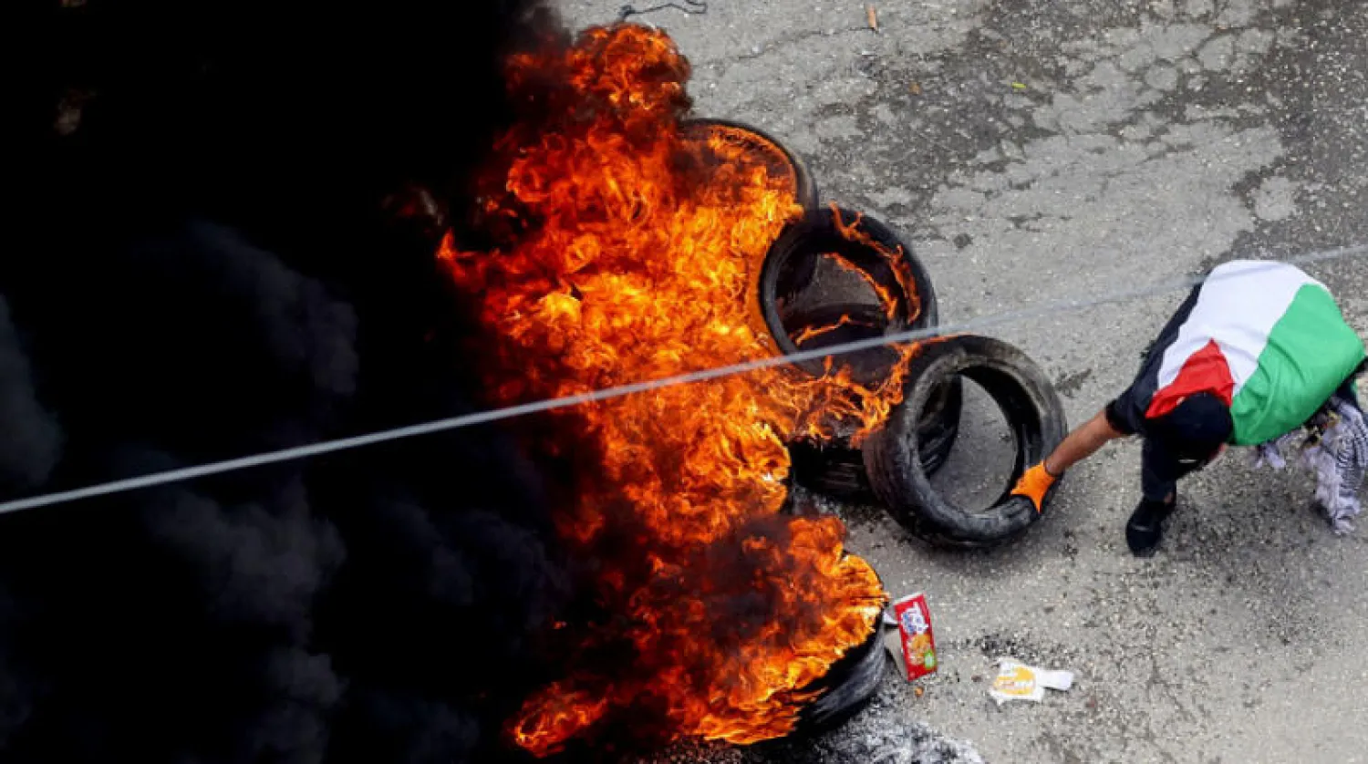 متظاهر فلسطيني يلقي بإطار مشتعل احتجاجاً على مسيرة للمستوطنين إلى بؤرة حومش العشوائية في قرية برقة شمال الضفة (أ.ف.ب)