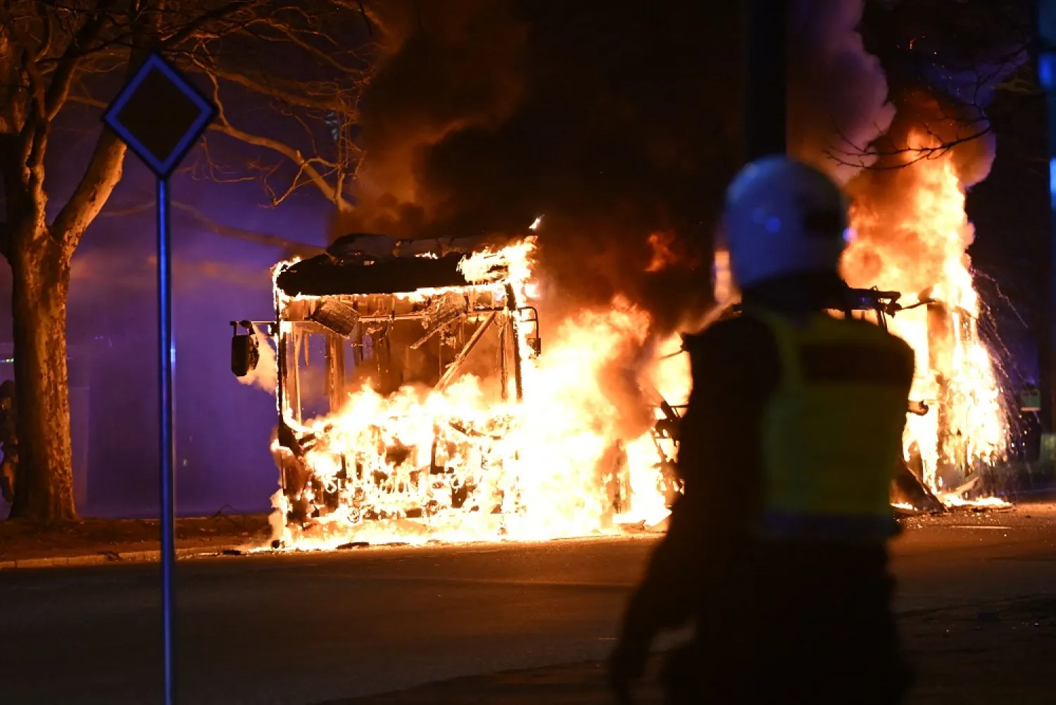 An anti-riot police officer stands next to a city bus burning in Malmo late April 16, 2022. (TT News Agency/AFP)