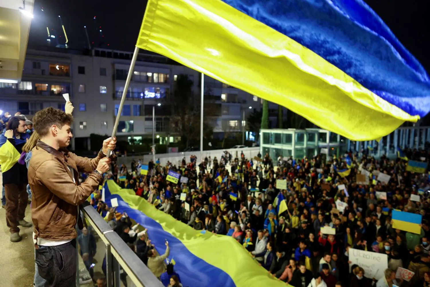 A man waves a flag from a balcony in front of demonstrators attending a rally in support of Ukraine, after Russia launched a massive military operation against Ukraine, in Tel Aviv, Israel, February 26, 2022. (Reuters)