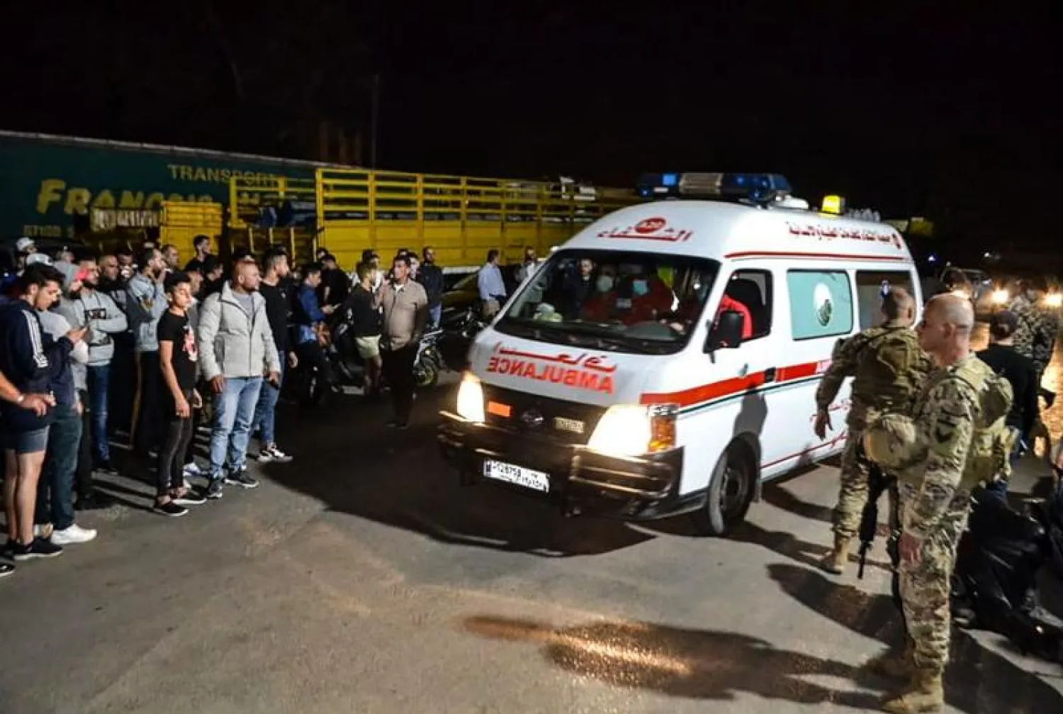 جنود لبنانيون ومواطنون عند مدخل ميناء طرابلس بينما تحمل سيارة إسعاف ناجين من حادث غرق الزورق (أ.ف.ب)