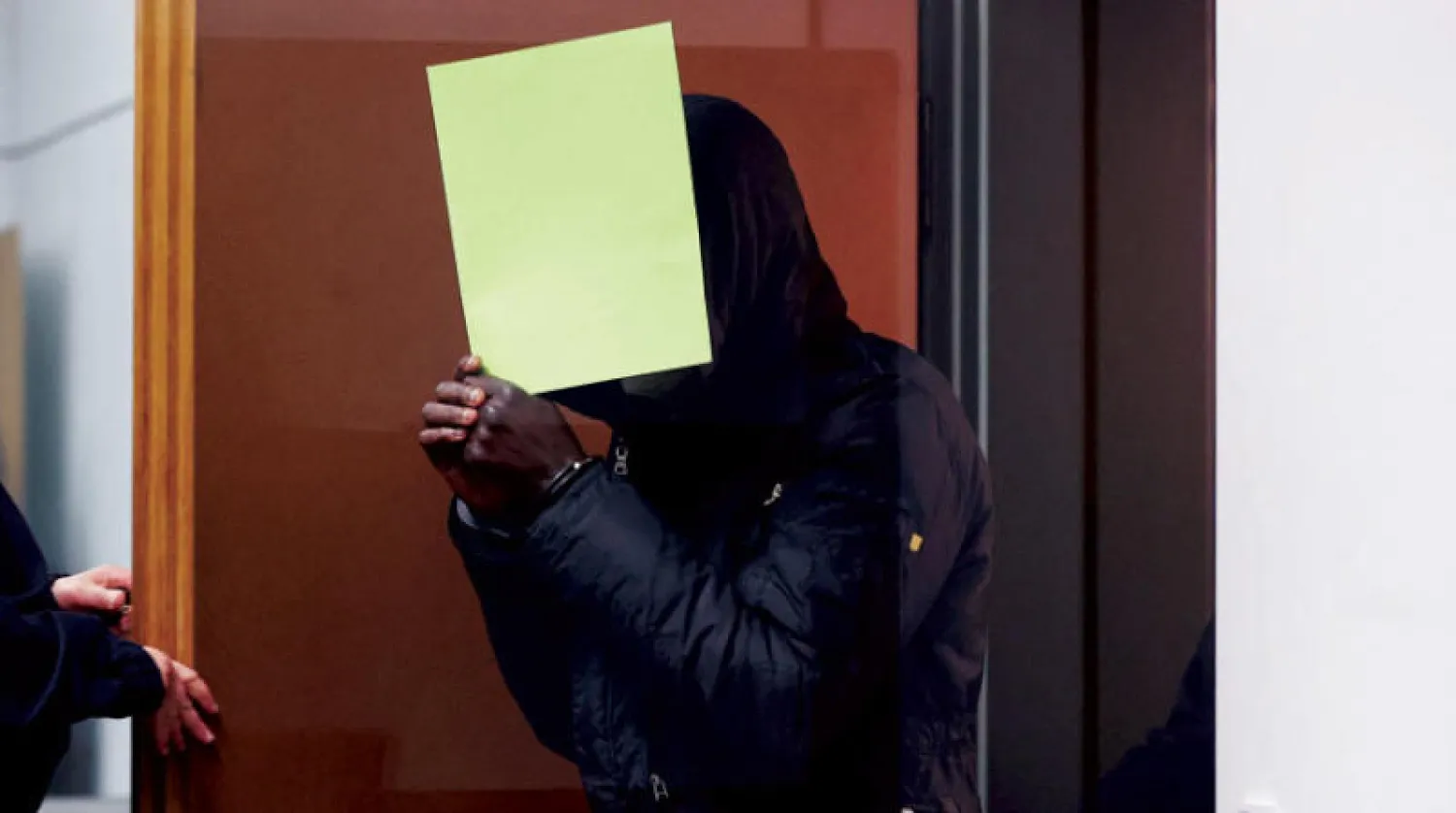 المتهم الغامبي باي لوي، المتهم بارتكاب جرائم ضد الإنسانية والقتل يخفي وجهه خلف ملف عند وصوله إلى قاعة المحكمة في تسيله بشمال ألمانيا عند افتتاح محاكمته أمس (أ.ف.ب)