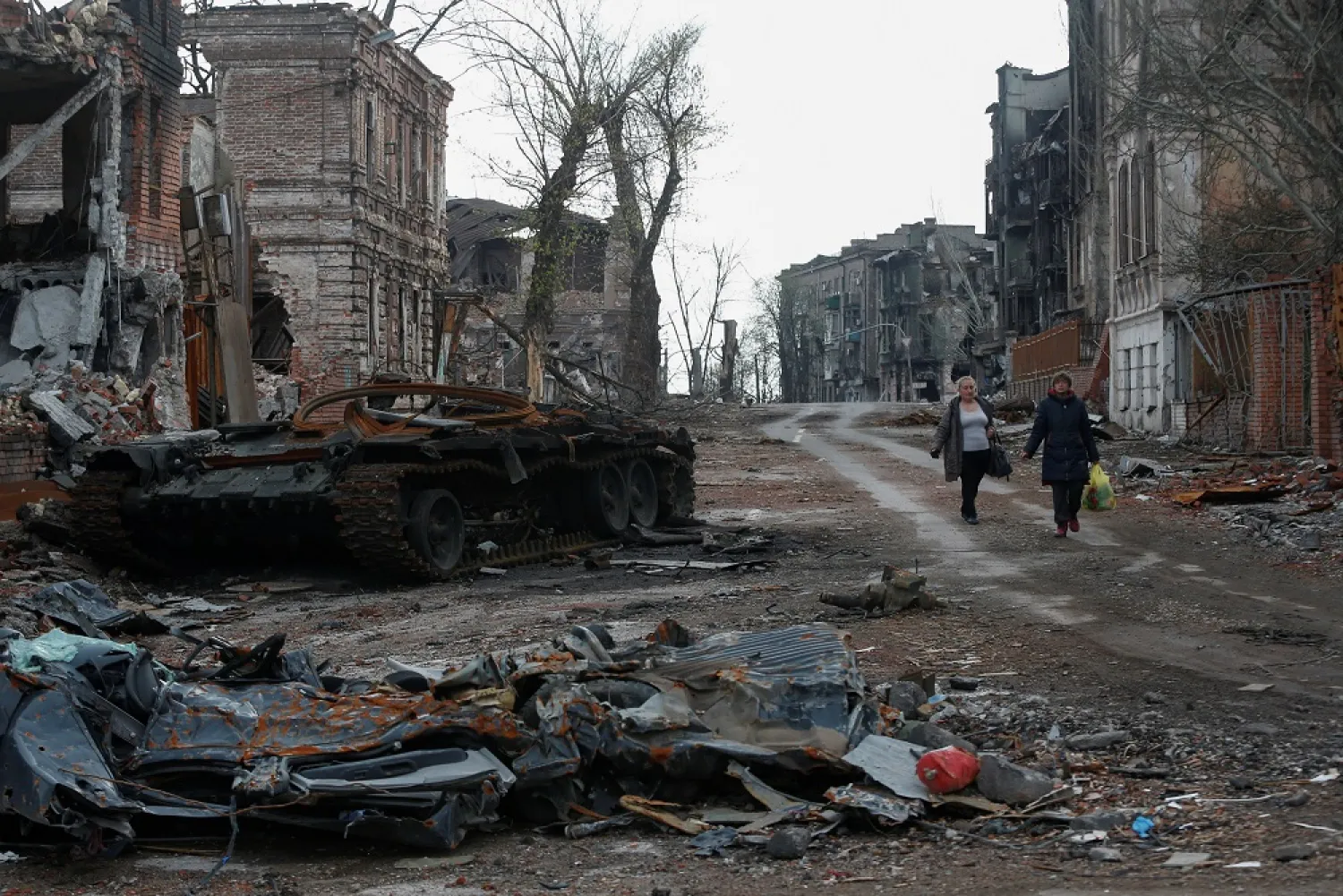 People walk near a destroyed tank and damaged buildings in the course of Ukraine-Russia conflict in the southern port city of Mariupol, Ukraine April 22, 2022. (Reuters)