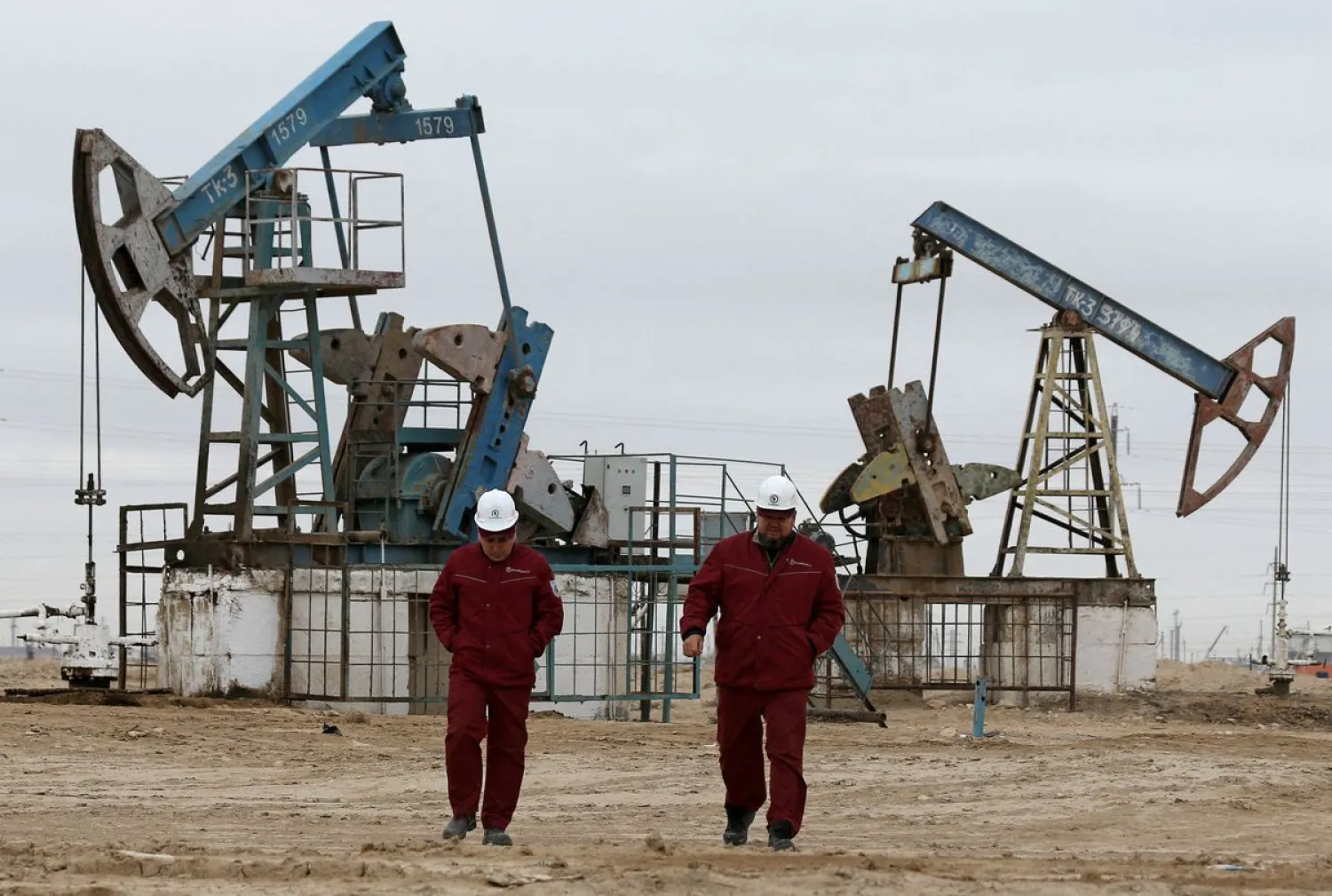 Workers walk as oil pumps are seen in the background in the Uzen oil and gas field in the Mangistau Region of Kazakhstan November 13, 2021. REUTERS/Pavel Mikheyev